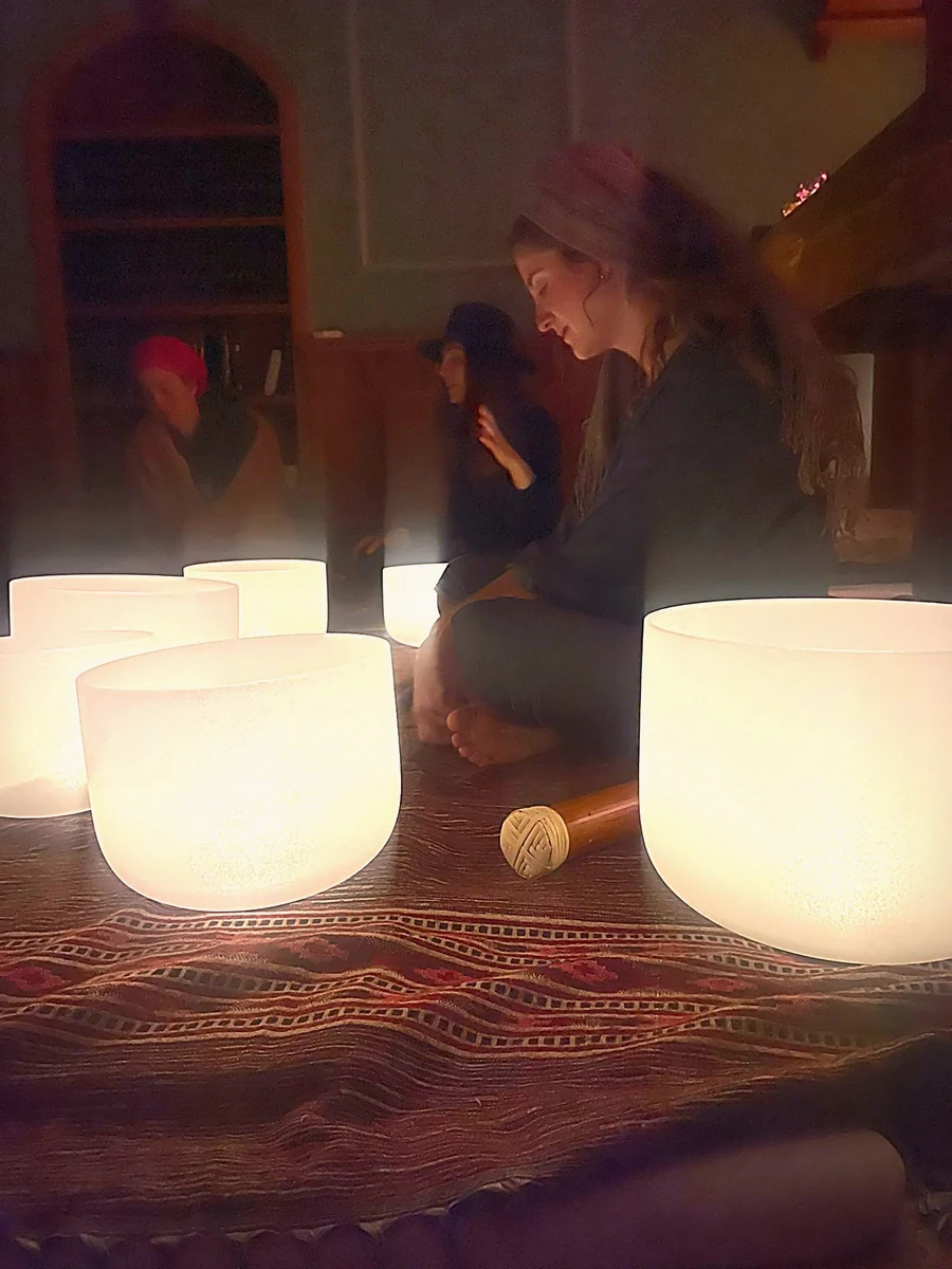Glowing crystal singing bowls with Tanya seated in candlelight